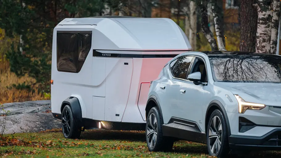 Der Karoo Adventure Camper im Zugbetrieb mit einem Polestar 3 statisch von schräg vorne rechts auf einer Wiese vor Birken.