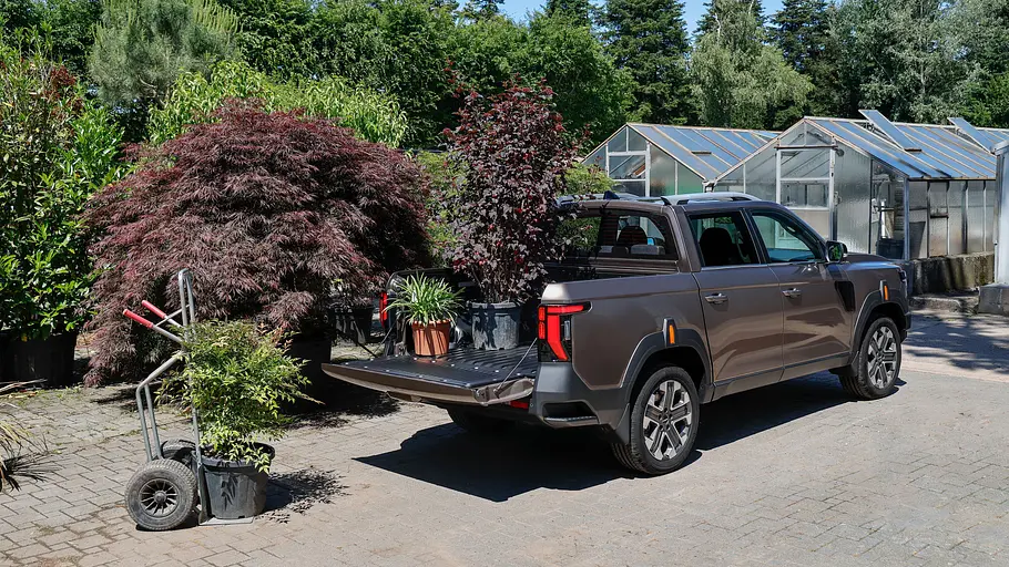 Der KGM Musso (2026) statisch von schräg hinten rechts auf dem Parkplatz eines Gartencenters. Auf der Ladefläche stehen Topfpflanzen.