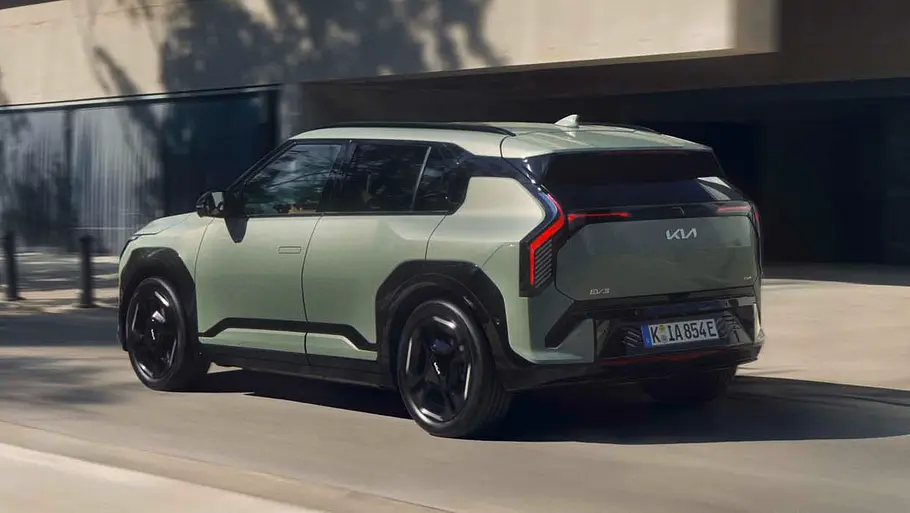 Kia EV3 Allrad News Der Kia EV3 mit Allradantrieb fahrend von schräg hinten links in einem städtischen Umfeld.