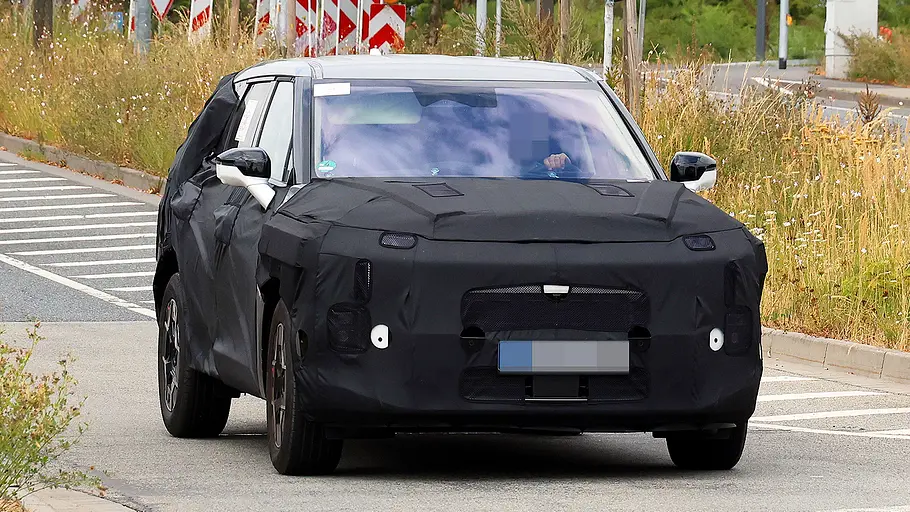 Blick von schräg vorne auf den fahrenden Erlkönig des Kia EV5 Facelift (2026).