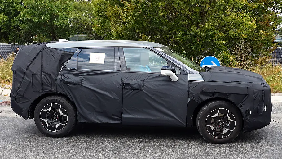Blick von der Seite auf den fahrenden Erlkönig des Kia EV5 Facelift (2026).