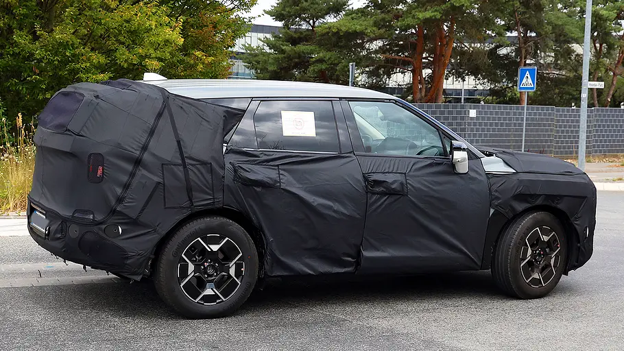 Blick von der Seite auf den fahrenden Erlkönig des Kia EV5 Facelift (2026).