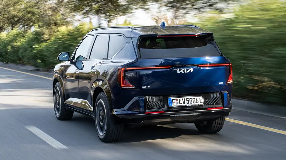 Der Kia EV5 fährt auf einer Straße, von hinten links fotografiert.