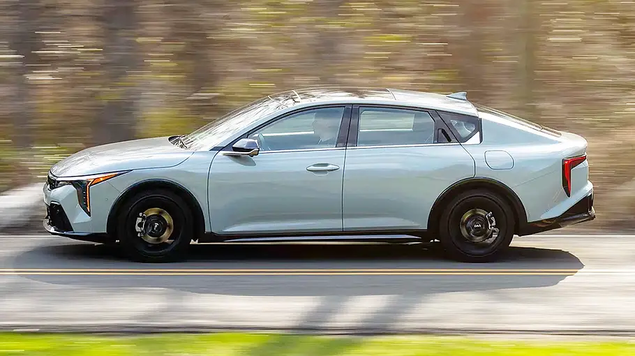 Der Kia K4 fährt auf einer Landstraße, von links fotografiert.