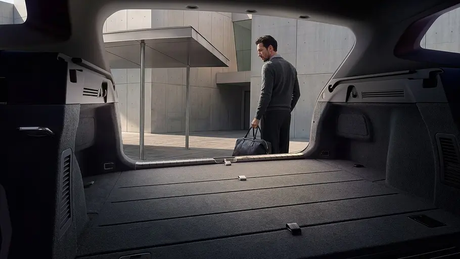 Kia K4 Sportswagon Firmenwagen Blick aus dem Kofferraum des Kia K4 Sportswagon durch die geöffnete Heckklappe. Eine Person mit einer Tasche steht außen am Fahrzeugheck.