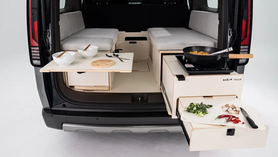 Die VanLab-Campingbox im Heck des Kia PV5 mit ausgeklapptem Tisch und ausgezogener Schublade.
