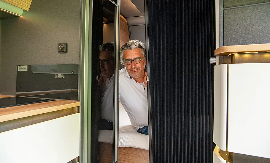 Knaus Azur 500 FU (2022) Knaus Azur 500 FU (2022) Wohnraum; Person blickt durch halb geschlossene Falttür aus dem Schlafbereich heraus
