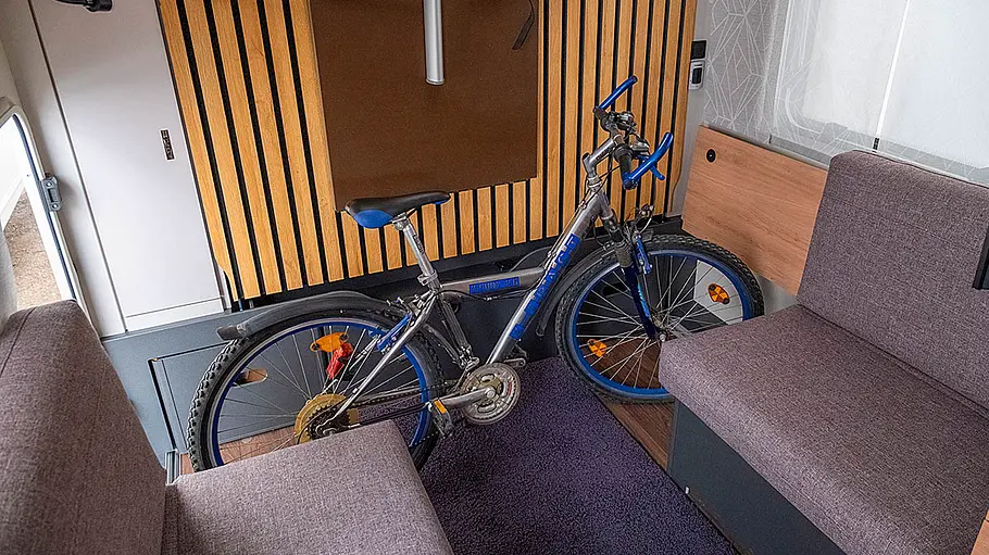 Ansicht des Wohnraums des Knaus Yaseo 340 PX. Ein Fahrrad steht hinter der geöffneten Garagenluke im hinteren Bereich der Sitzgruppe.