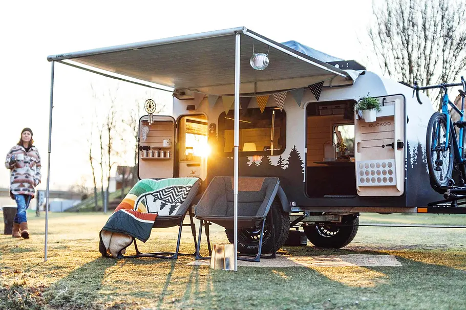 Das Bild zeigt den Kuckoo Camper Bruno (2026) auf einem Stellplatz, davor stehen zwei Stühle.