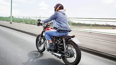 Eine Frau fährt mit dem Motorrad über eine Brücke, von hinten links fotografiert. - Foto: Imago