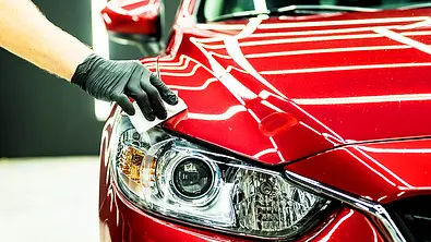 Hand beim Abwischen eines roten Autos zur Lackversiegelung, fotografiert von vorne. - Foto: iStock/romaset