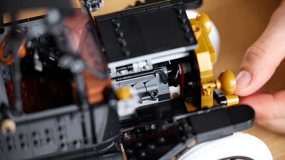 Der Motor des Lego Icons Ford Model T im Detail. Eine Hand betätigt die Anlasskurbel unter dem Kühlergrill des Lego-Modells.