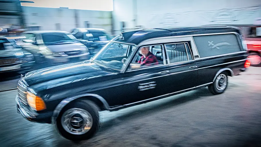 Mercedes W123 Leichenwagen fahrend von der Seite fotografiert.  