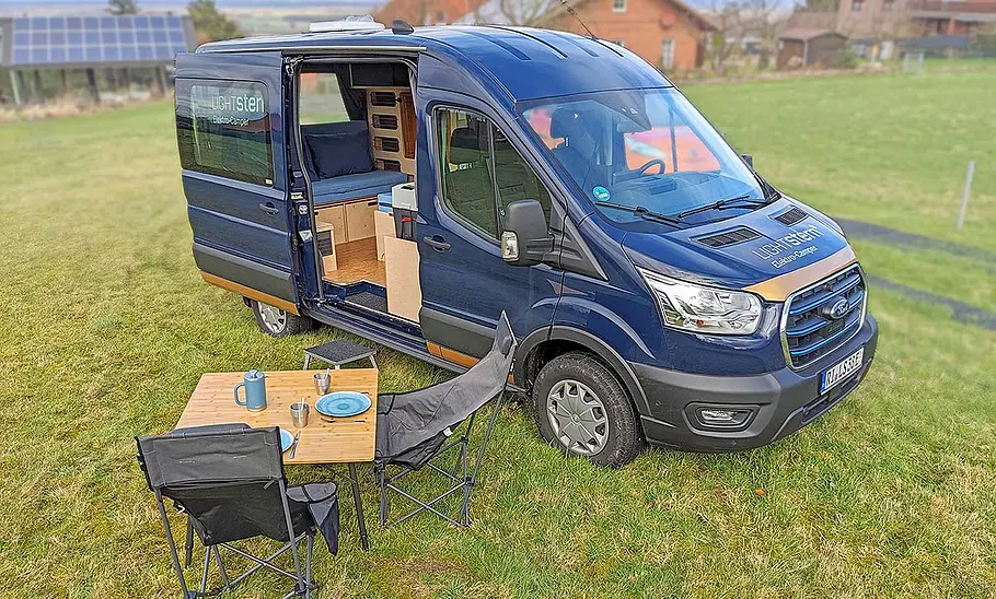Lightstern Polaris (2025) Das Bild den Lightstern Polaris (2025) stehend von schräg vorne rechts fotografiert. Vor der geöffneten rechten Schiebetüre stehen Campingmöbel.