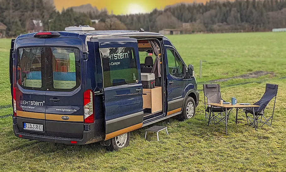Lightstern Polaris (2025) Das Bild den Lightstern Polaris (2025) stehend von schräg hinten rechts fotografiert. Vor der geöffneten rechten Schiebetüre stehen Campingmöbel.