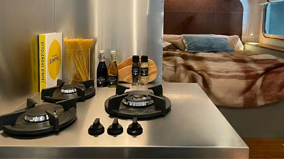 Lume Nordic Die Innenküche des Lume Nordic mit Dreiflammen-Gaskocher, auf der Arbeitsfläche liegen das Kochbuch Ottolenghi Simple, ein Vorratsglas mit ungekochten Spaghetti, Ölflaschen und Gewürzgläser.