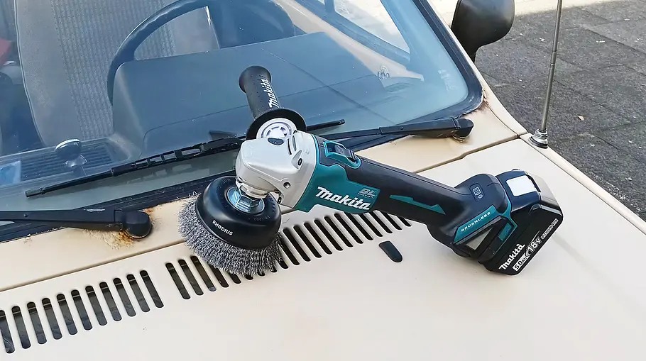 Makita Akku-Flex DGA504 Die Makita Akku-Flex DGA504 liegt auf der angerosteten Motorhaube eines älteren VW Polo.
