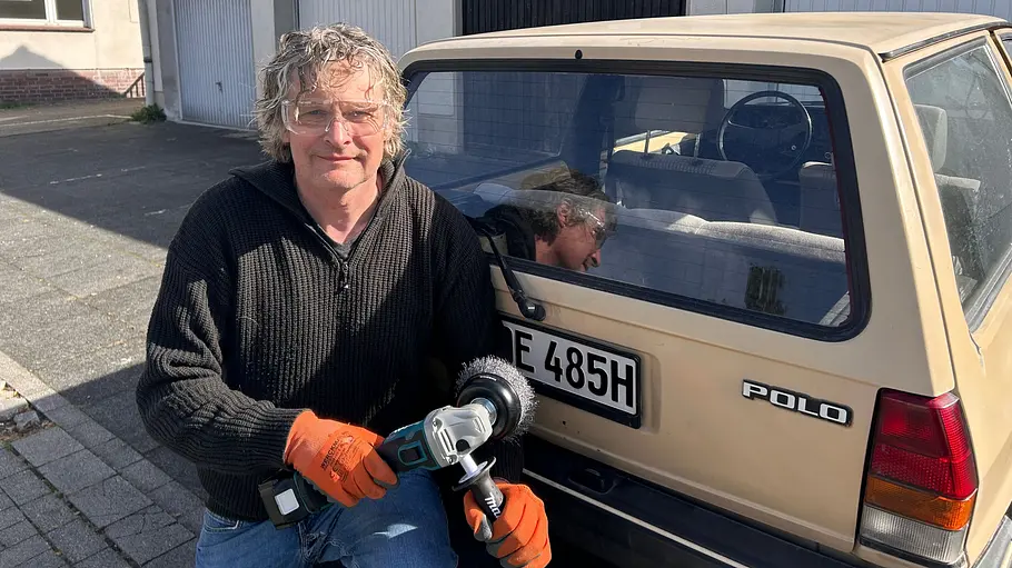 Makita Akku-Flex DGA504 Ein Produkttest-Redakteur kniet mit Makita-Winkelschleifer vor dem Heck eines Oldtimers (VW Polo 86 C), der als Versuchsobjekt dient.