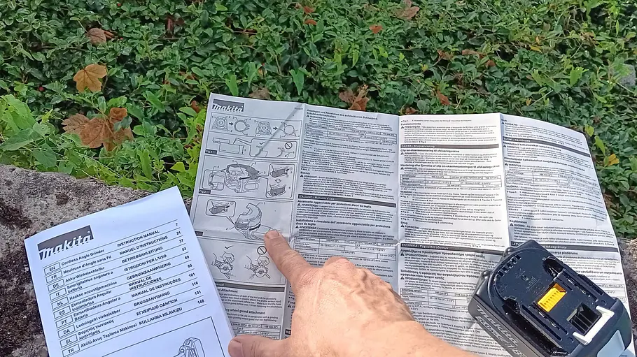 Makita Akku-Flex DGA504 Der Finger eines Testers fährt über die Bedienungsanleitung.