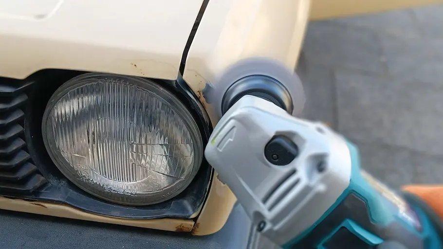 Makita Akku-Flex DGA504 Die Detailaufnahme zeigt die Makita Akku-Flex DGA504 im Einsatz im Bereich des linken Frontscheinwerfers eines älteren VW Polo.