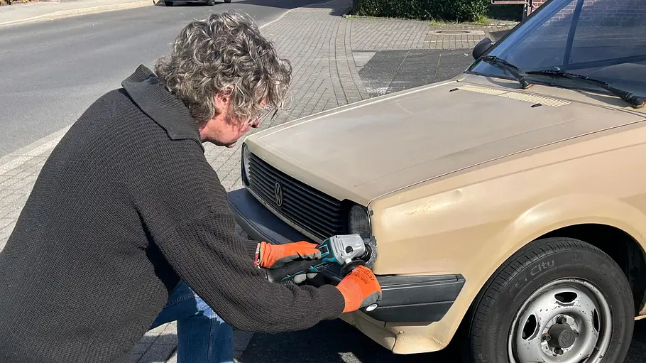 Makita Akku-Flex DGA504 Die Detailaufnahme zeigt einen Tester mit der Makita Akku-Fkex DGA504 beim Einsatz am Frontcheinwerfer eines älteren VW Polo.