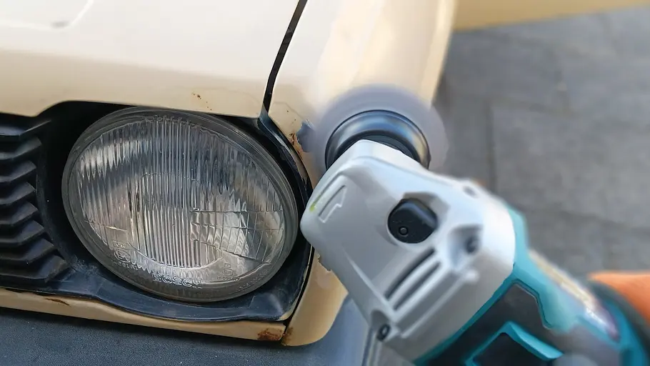 Makita Akku-Flex DGA504 Die Detailaufnahme zeigt die Makita Akku-Flex DGA504 im Einsatz im Bereich des linken Frontscheinwerfers eines älteren VW Polo.