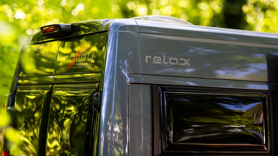 Malibu Relax 640 LE R Der Schriftzug auf der hinteren rechten Ecke des Malibu Relax im Detail. Auf der Karosserie spiegelt sich ein Wald.