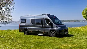 Der Malibu Relax Van statisch von schräg vorne links auf einer Wiese vor einem See. - Foto: Malibu