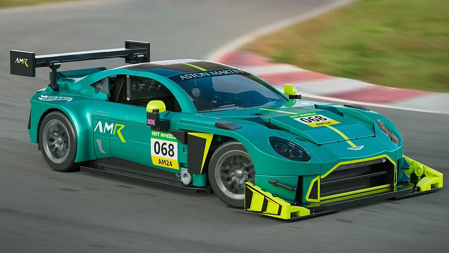 Der Mattel Brick Shop Aston Martin Vantage GT3 von schräg vorne links digital beschleunigt vor einem Rennstrecken-Hintergrund.