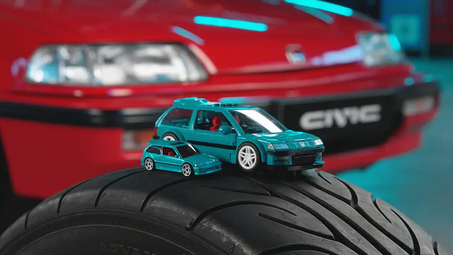 Der Honda Civic EF von Mattel Brick Shop auf einem aufgestellten Autoreifen vor einem echten Honda Civic EF stehend.