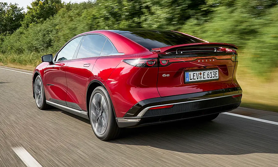 Der Mazda6e (2025) fährt über eine Landstraße, fotografiert von schräg hinten.