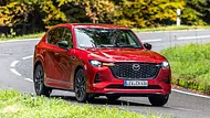 Der Mazda CX-60 fährt durch eine Linkskurve im Wald, fotografiert von schräg vorne. - Foto: Frank Ratering