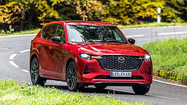 Der Mazda CX-60 fährt durch eine Linkskurve im Wald, fotografiert von schräg vorne. - Foto: Frank Ratering