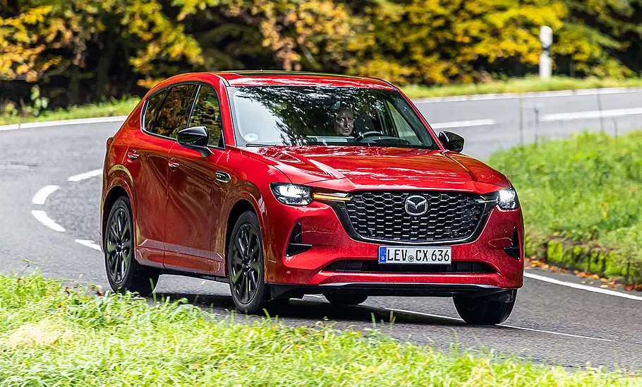 Der Mazda CX-60 fährt durch eine Linkskurve im Wald, fotografiert von schräg vorne.