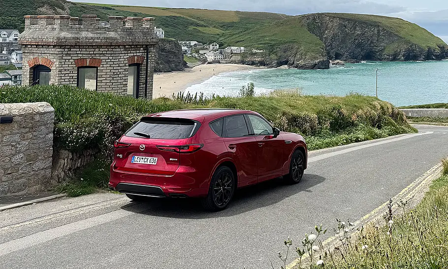 Der Mazda CX-60 steht vor der Kulisse eines britischen Küstenstreifens, fotografiert von schräg hinten.