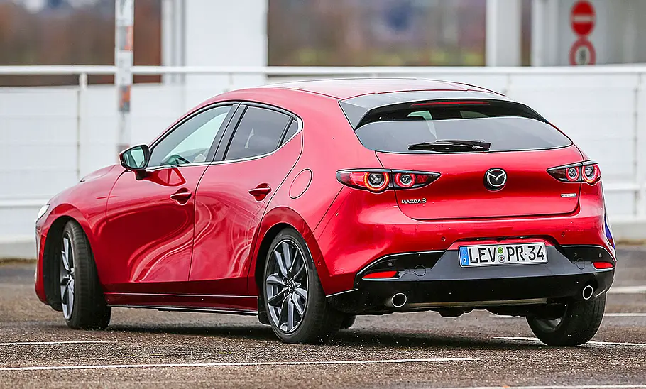 Der Mazda3 (2019) fährt auf einer Straße, von hinten links fotografiert.