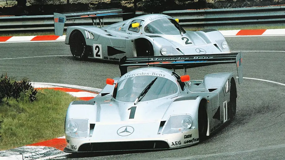 Blick von vorne auf zwei Mercedes C11, die auf einer Rennstrecke eine enge Kurve passieren.