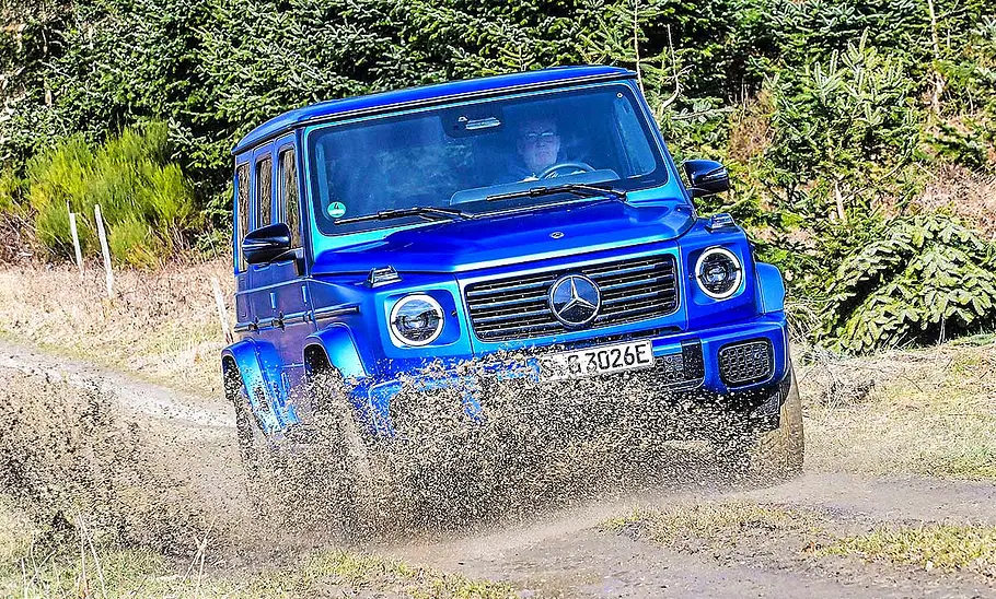 Mercedes G 580 EQ Blick von schräg vorne auf den fahrenden Mercedes G 580 EQ, der gerade durch eine tiefe Matschpfütze fährt.