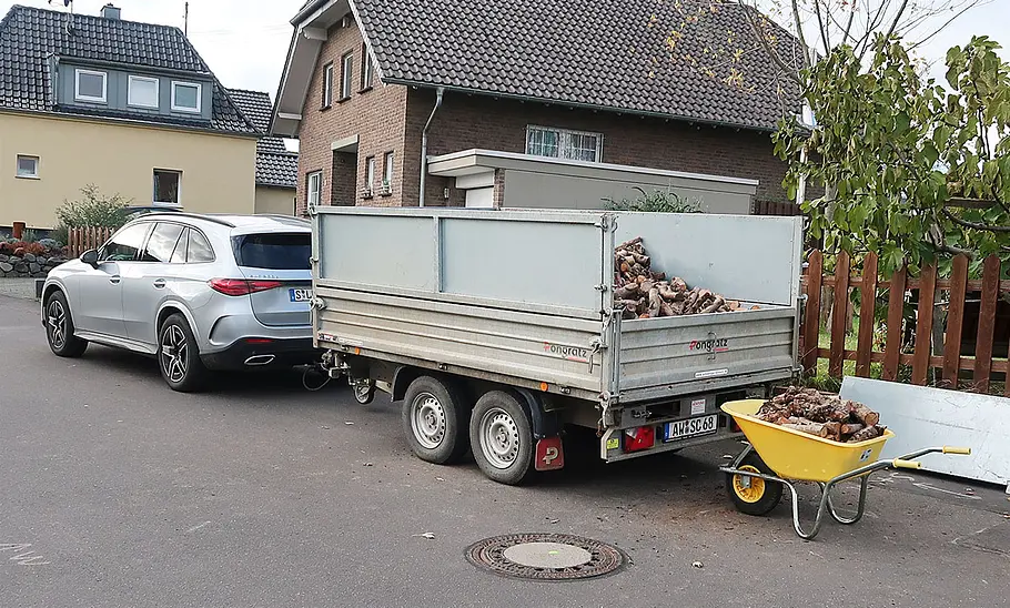 Mercedes GLC 300 d 4Matic Der Mercedes GLC 300 d 4Matic hat einen zweiachsigen Anhänger angekoppelt, der mit Brennholz beladen wird.