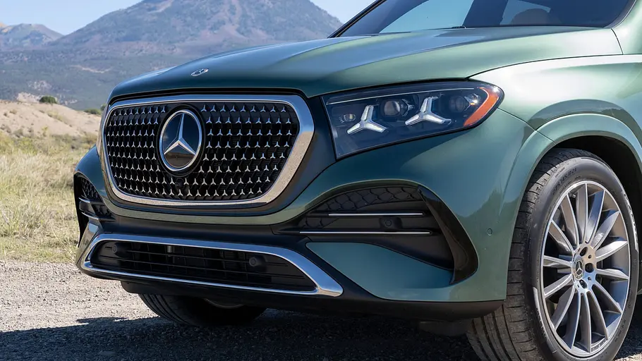Mercedes GLE 580 4Matic Modellpflege Fahrbericht Die Front eines grünen Mercedes-Benz GLE mit großem Kühlergrill vor einer Berglandschaft.