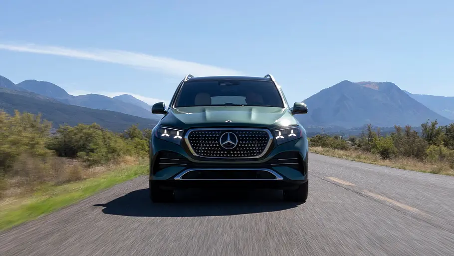 Mercedes GLE 580 4Matic Modellpflege Fahrbericht Ein grüner Mercedes GLE fährt frontal auf einer Landstraße, umgeben von Sträuchern und Bergen unter blauem Himmel.