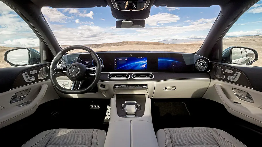 Mercedes GLE 580 4Matic Modellpflege Fahrbericht Der Mercedes GLE Innenraum hat helle Sitze und ein breites digitales Armaturenbrett. Durch die Fenster ist eine karge Landschaft sichtbar.