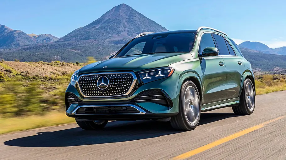 Mercedes GLE 580 4Matic Modellpflege Fahrbericht Ein grüner Mercedes GLE fährt auf einer Straße durch eine bergige Landschaft unter blauem Himmel.