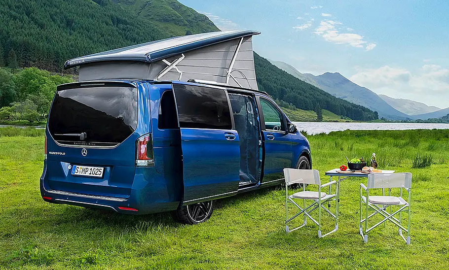 Mercedes Marco Polo (2026) Das Bild zeigt den Mercedes Marco Polo (2024) stehend von schräg hinten rechts fotografiert. Das Aufstelldach und die rechte Schiebetüre sind geöffnet, Stühle und Tisch stehen vor dem Camper.