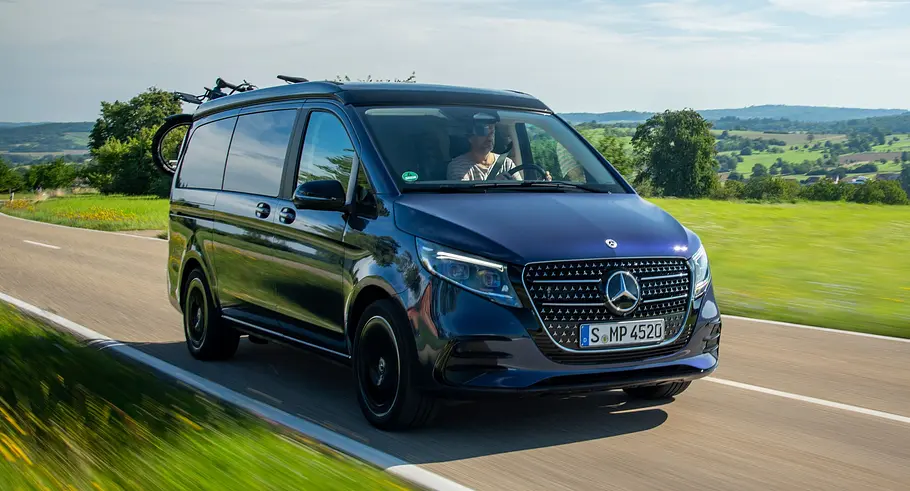 Die Mercedes V-Klasse Marco Polo fährt auf einer Straße, fotografiert von vorne schräg auf.