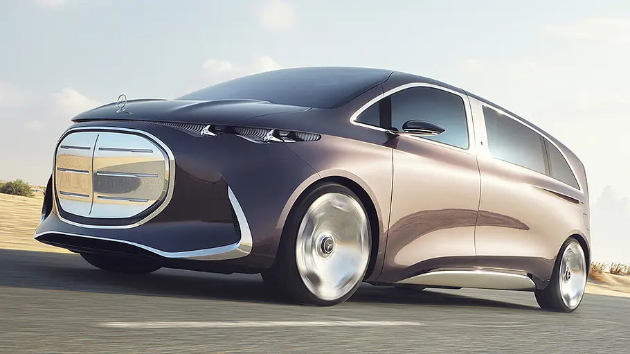 Der Mercedes Vision V (2025) fährt vor Wüsten- und Skyline-Hintergrund durch Dubai, von vorne links fotografiert.