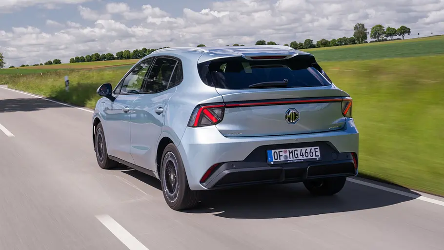 MG4 EV Urban Der MG4 EV Urban fährt auf einer Landstraße, von hinten links fotografiert.