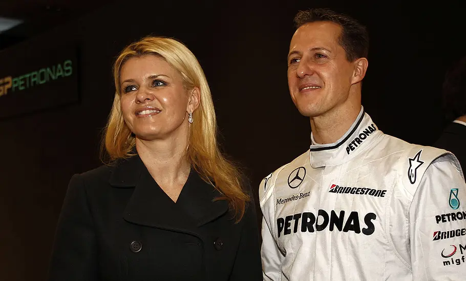 Michael und Corinna Schumacher nebeneinander stehend vor dunklem Hintergrund.
