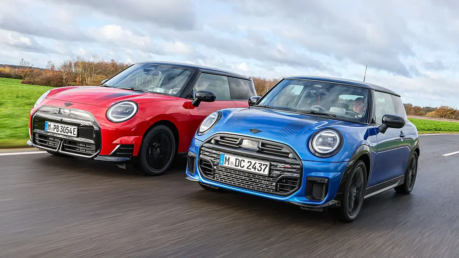Mini Cooper S und Cooper SE Die beiden Mini Cooper fahren nebeneinander auf einer Landstraße und wurden von vorne schräg fotografiert.
