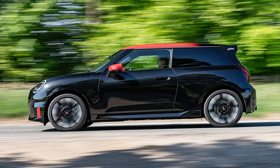 Der Mini JCW Electric (2025) fährt über eine Landstraße, fotografiert von der Seite.